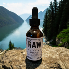 Load image into Gallery viewer, A bottle of Raw By Nature Beard Oil overlooking a mountain and water