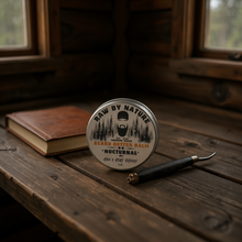 Load image into Gallery viewer, Beard butter balm container labeled 'Raw by Nature' on a wooden surface with a book and tool.