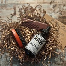Load image into Gallery viewer, A bottle of Raw By Nature Bear oil with a brush and comb on top of brown crinkled paper