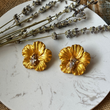 Load image into Gallery viewer, Gold hibiscus earrings on on ceramic tile with flowers

