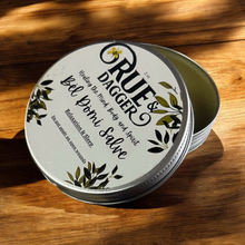 Load image into Gallery viewer, Tin of Rue &amp; Dagger Balm on a dark wooden surface
