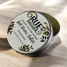 Load image into Gallery viewer, Tin of Rue &amp; Dagger Balm on a wooden surface
