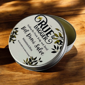 Tin of Rue & Dagger Balm on a dark wooden surface