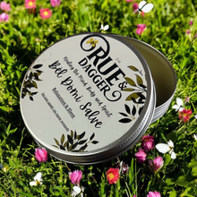 Load image into Gallery viewer, Tin of Rue &amp; Dagger Bel Domi Salve on a grassy background with flowers
