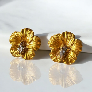 Gold hibiscus earrings on a see through countertop 
