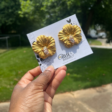 Load image into Gallery viewer, Gold hibiscus earrings with greenery in the background 
