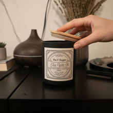 Load image into Gallery viewer, Hand holding a wooden wick over a candle labeled 'She Wit It' on a table.
